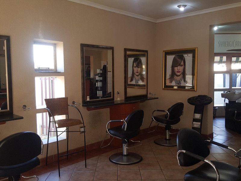 A commercial hair salon interior featuring multiple styling stations with wall-mounted mirrors, built-in vanity counters, and dedicated hair washing basins.
