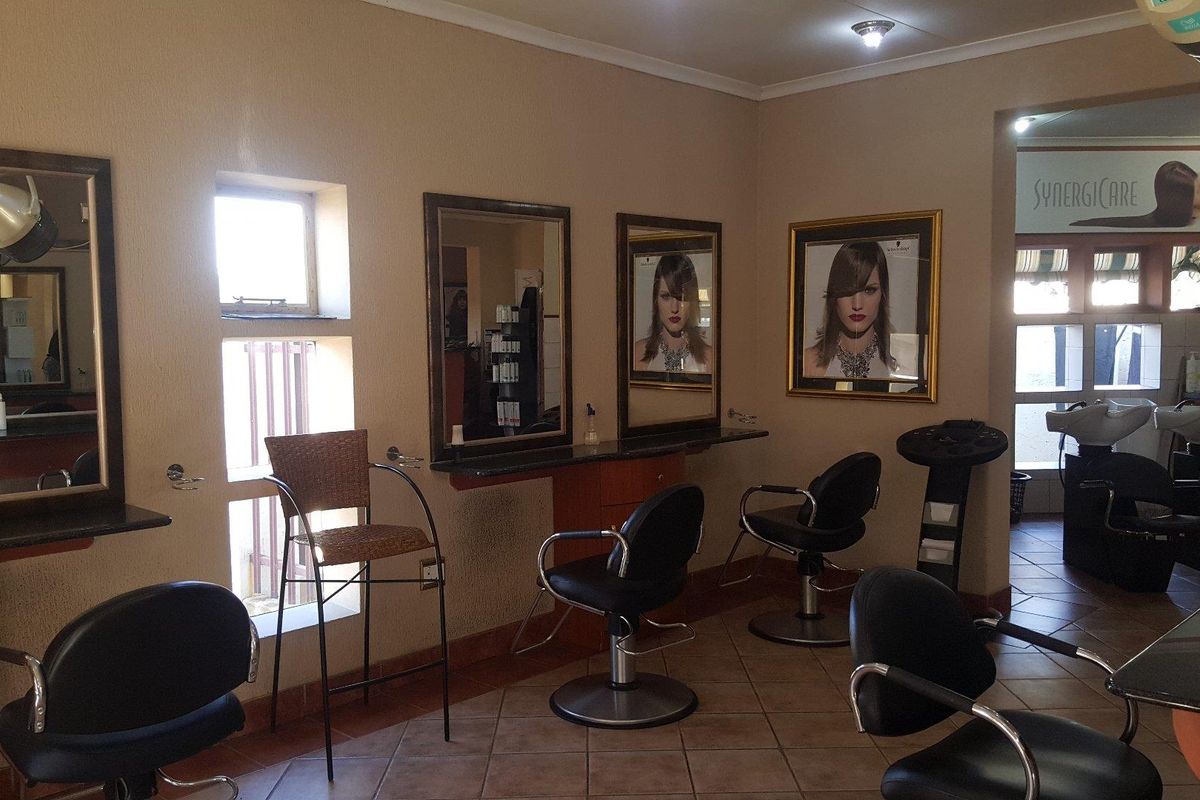 A commercial hair salon interior featuring multiple styling stations with wall-mounted mirrors, built-in vanity counters, and dedicated hair washing basins.