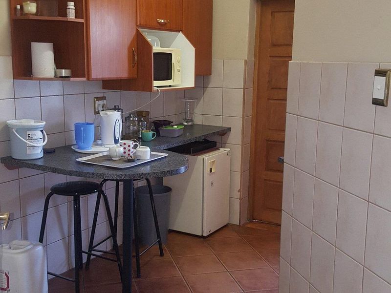 A compact kitchen area featuring laminate cabinetry, tiled splashbacks, ceramic floor tiles, and a built-in breakfast bar counter.