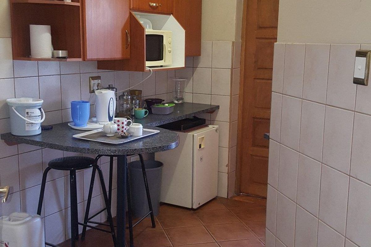 A compact kitchen area featuring laminate cabinetry, tiled splashbacks, ceramic floor tiles, and a built-in breakfast bar counter.