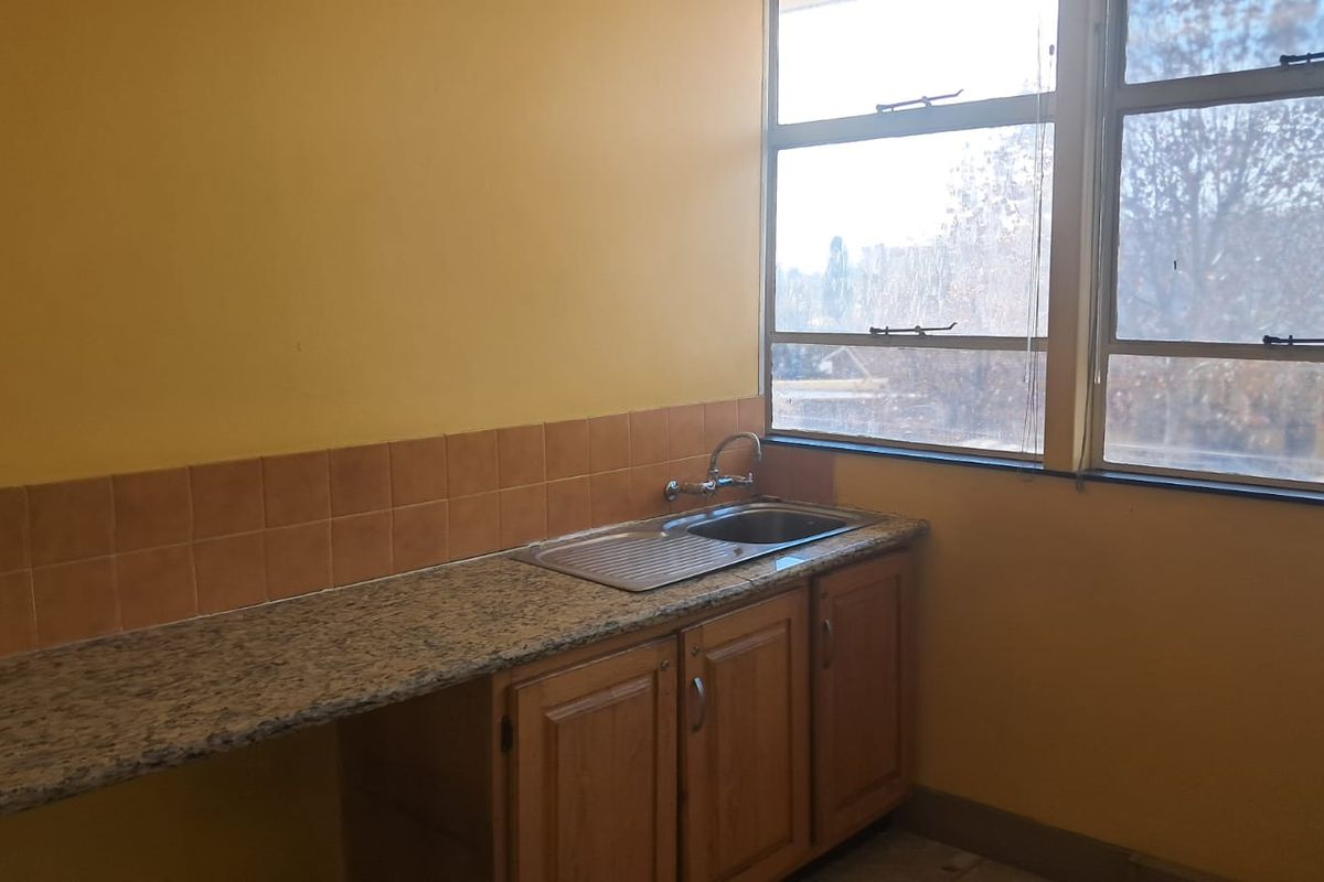 A functional kitchenette area featuring granite countertops, a stainless steel sink, tiled backsplash, and wooden cabinetry with natural light from large windows.