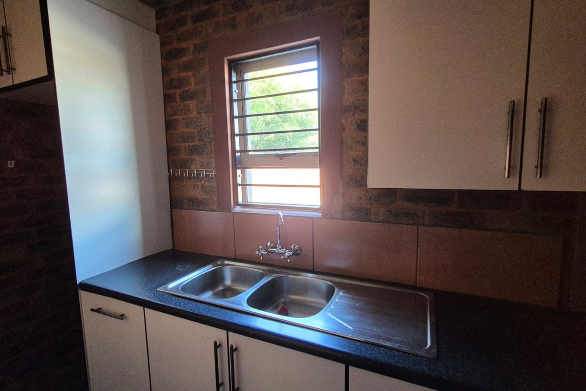 A functional kitchen area featuring a double stainless steel sink, built-in cabinetry, and an exposed brick wall finish.