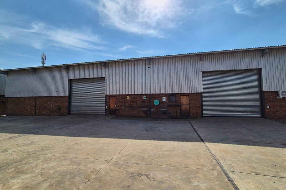 Industrial warehouse exterior featuring large roller shutter doors, brick and metal cladding construction, and a spacious concrete yard area.