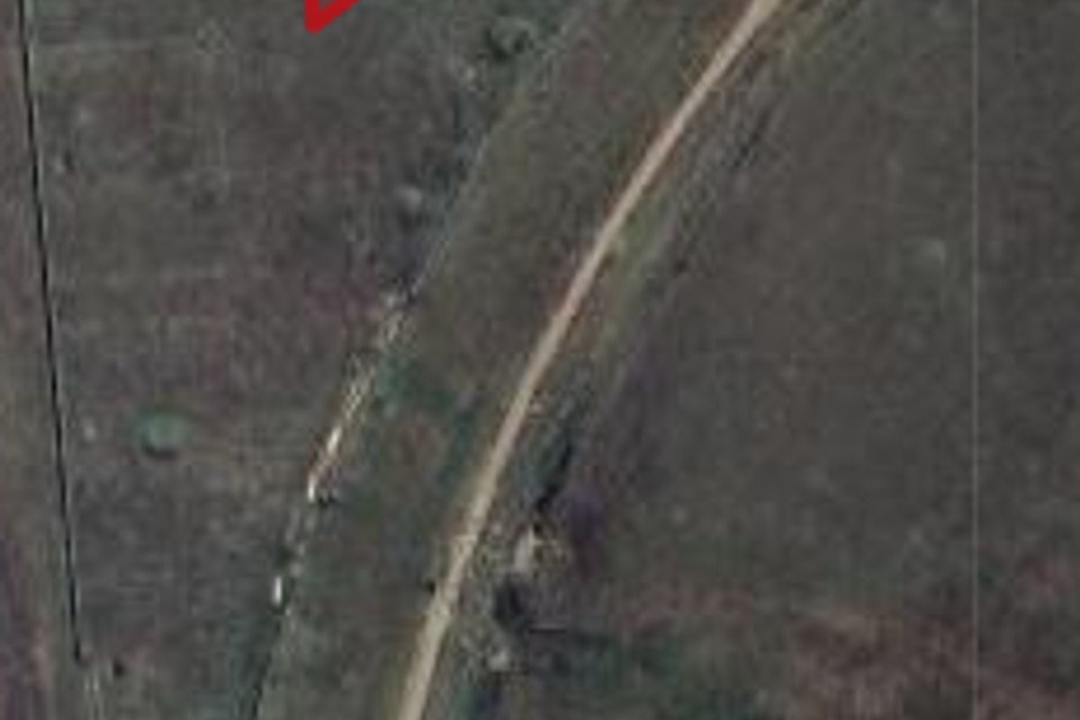 Aerial view of a vacant commercial land plot with perimeter fencing and adjacent unpaved road access.