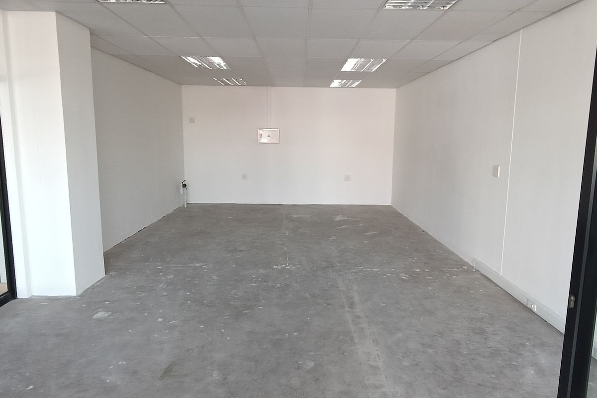 An empty, open-plan commercial office space featuring a suspended ceiling, recessed lighting, and a glass partition wall, ready for tenant fit-out.