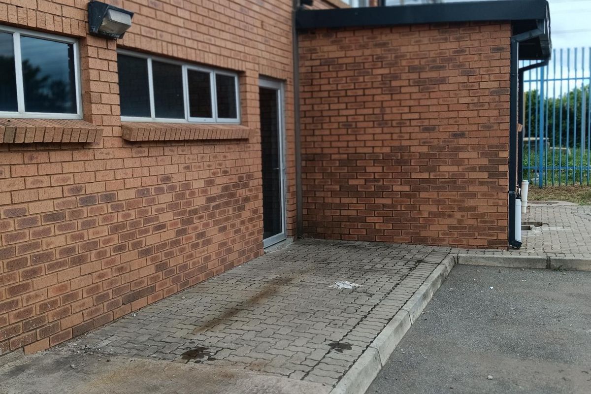Exterior view of an industrial brick building featuring paved access area, metal window frames, and security fencing.