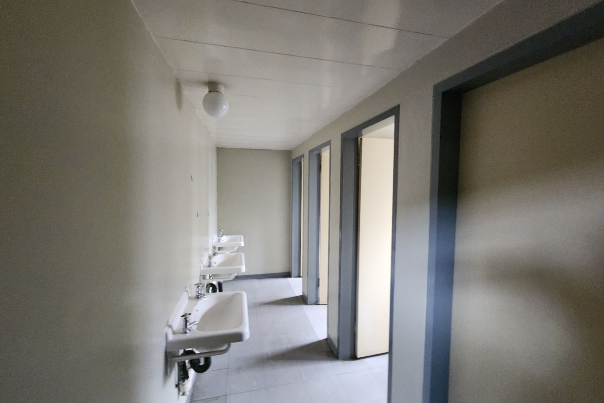A functional industrial washroom area featuring a row of wall-mounted ceramic basins and multiple access doors to individual stalls.
