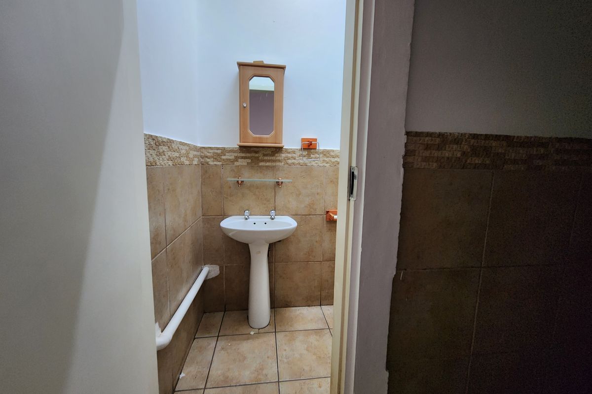 A compact bathroom featuring a pedestal basin, wall-mounted medicine cabinet, and tiled walls with a decorative border.