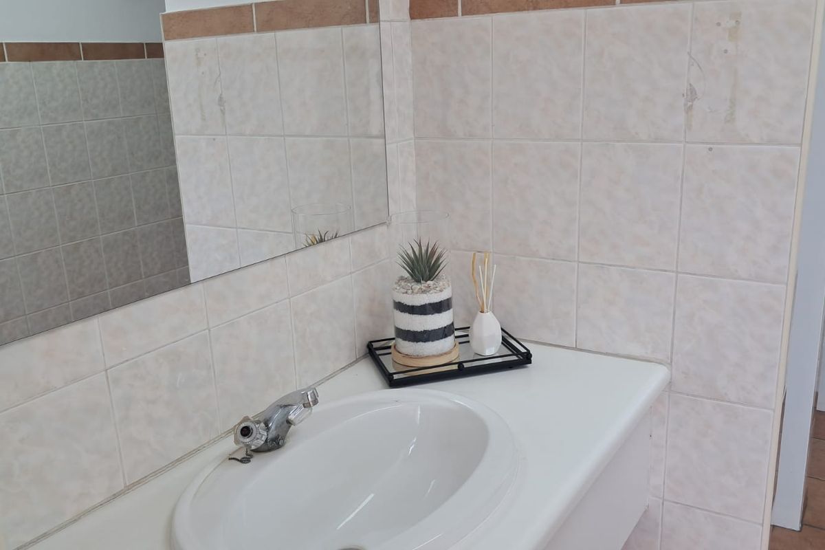 A functional office bathroom featuring a built-in vanity with a ceramic basin, chrome faucet, and wall-mounted mirror with tiled splashback.