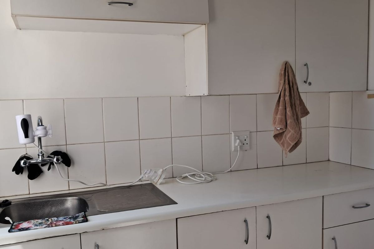 A functional office kitchenette featuring white cabinetry, a stainless steel sink, and tiled splashback, providing essential utility space for staff.
