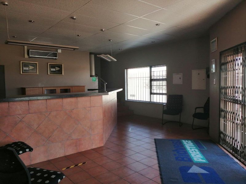 Commercial reception area featuring a built-in reception desk, tiled flooring, suspended ceiling, and secure access gate with security bars on windows.