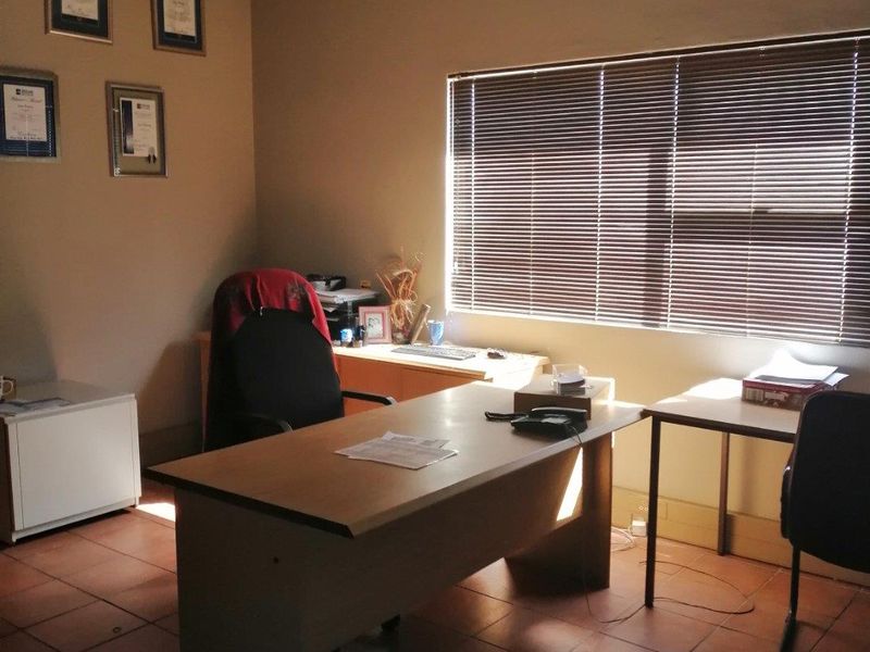 A functional commercial office space featuring ceramic tile flooring, a suspended ceiling, and venetian blinds providing natural light control.