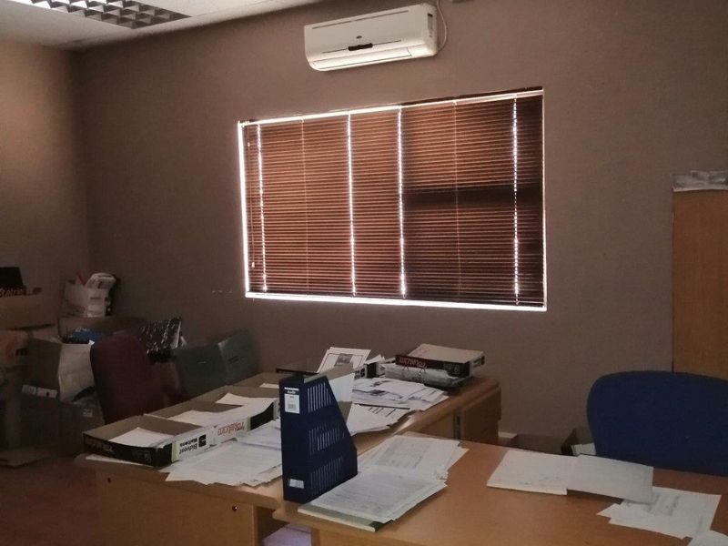 A functional office space featuring a suspended ceiling, recessed lighting, tiled floors, and a wall-mounted split-system air conditioning unit.