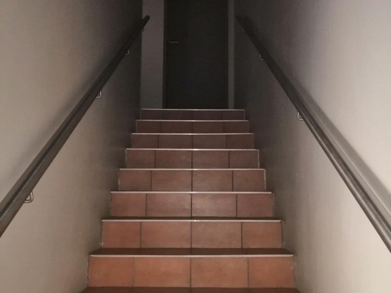 A simple interior staircase featuring tiled steps and dual metal handrails leading to a doorway.