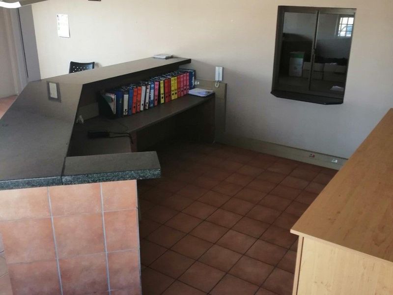 Commercial reception area featuring a built-in service desk, tiled flooring, and an internal service window, suitable for office or professional business use.