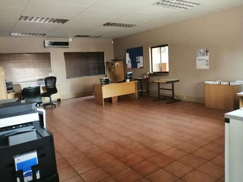 A functional commercial office space featuring ceramic tile flooring, a suspended ceiling with recessed lighting, and a wall-mounted air conditioning unit.
