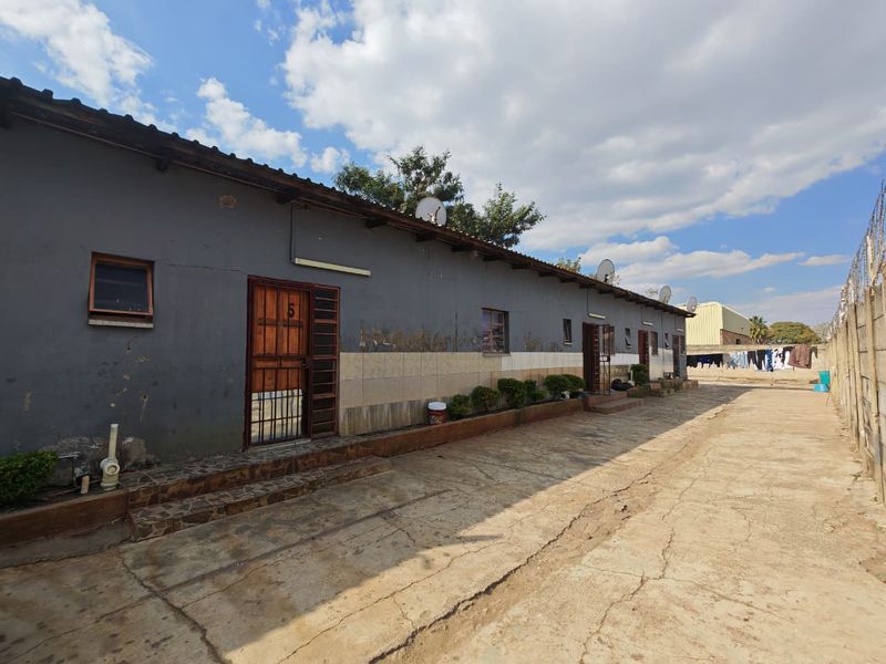 Rear exterior view of a commercial property featuring a long concrete driveway, multiple unit entrances, and a perimeter boundary wall.