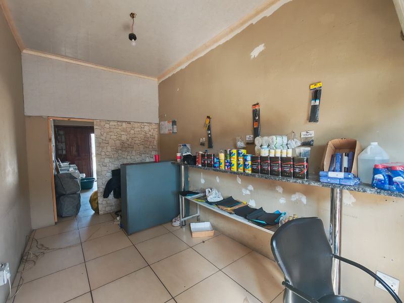 Commercial utility or retail space featuring tiled flooring, a stone-cladding accent wall, and a built-in service counter, currently requiring cosmetic repairs and wall finishing.