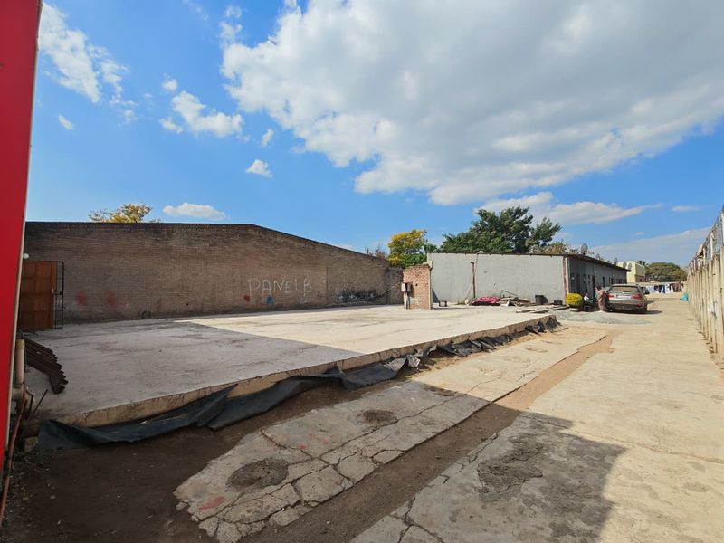 An expansive outdoor commercial yard area featuring a large concrete slab, brick boundary walls, and significant space for potential development or storage.