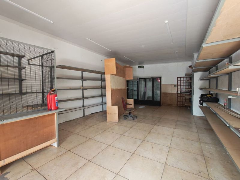 A vacant commercial retail space featuring tiled flooring, extensive built-in metal shelving, and fluorescent lighting, suitable for various business or storage applications.