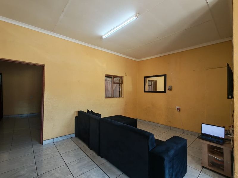 A living room featuring ceramic floor tiles and yellow painted walls, providing a functional space with direct access to an adjoining room.