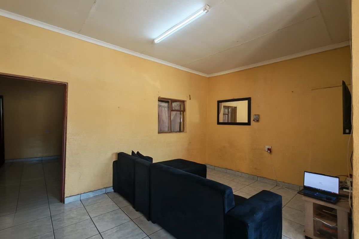 A living room featuring ceramic floor tiles and yellow painted walls, providing a functional space with direct access to an adjoining room.