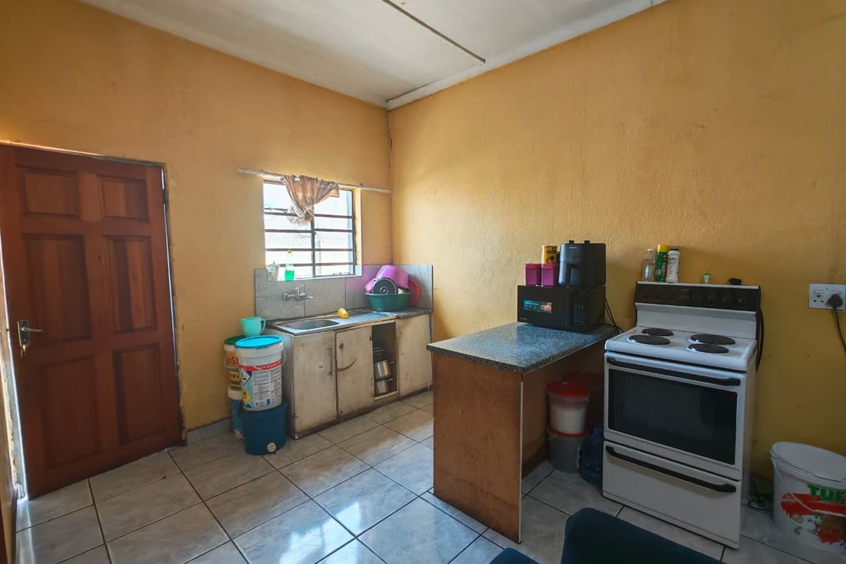 A functional kitchen area featuring tiled flooring, a stainless steel sink, and a freestanding stove, requiring cosmetic updates to improve its overall condition.