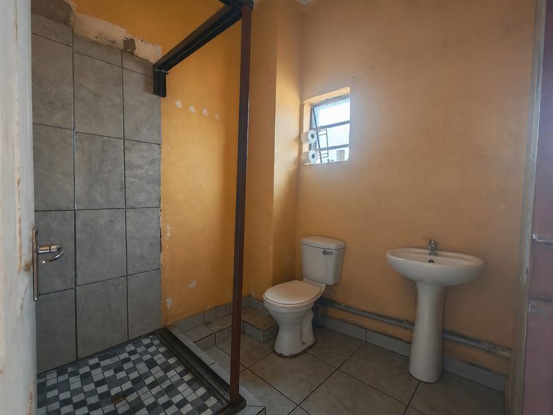 A dated bathroom featuring a pedestal basin, toilet, and shower enclosure with tiled finishes, requiring cosmetic updates and wall repairs.