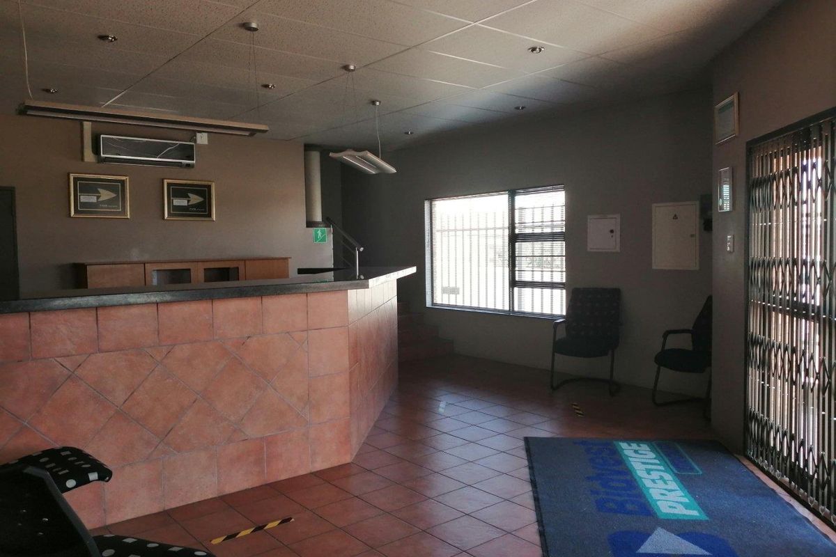 Commercial reception area featuring a built-in reception desk, tiled flooring, suspended ceiling, and secure access gate with security bars on windows.