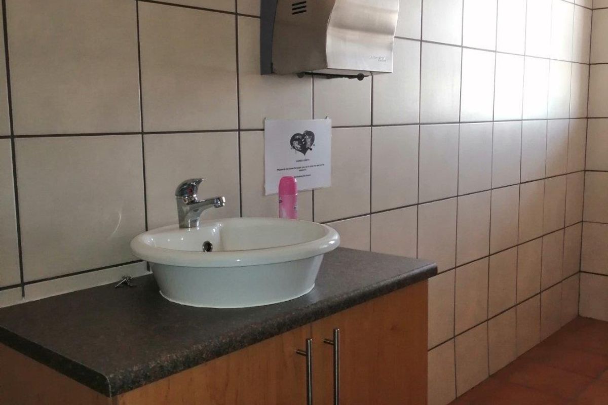 A functional commercial bathroom featuring a vanity cabinet with a ceramic basin, tiled walls, and a stainless steel paper towel dispenser.