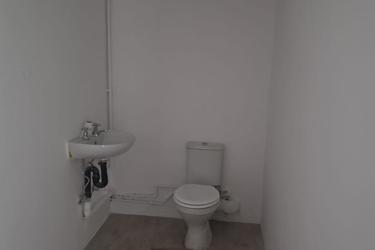 A basic, functional bathroom featuring a standard toilet and wall-mounted basin with exposed plumbing fixtures.