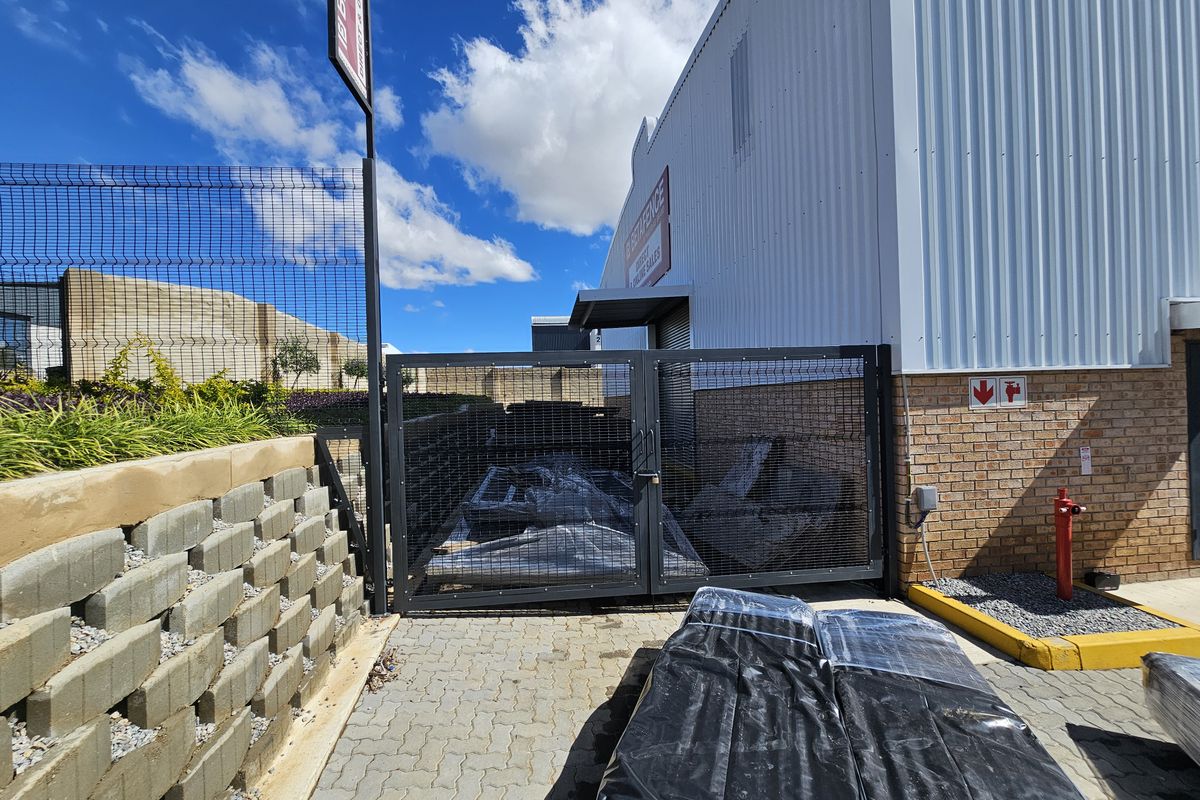 Exterior view of an industrial property featuring a secure gated yard area, brick and metal cladding, and a fire hydrant connection.
