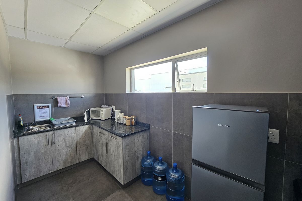 Compact industrial kitchenette featuring granite countertops, modern cabinetry, tiled splashbacks, and a drop-in sink, suitable for office or warehouse staff use.