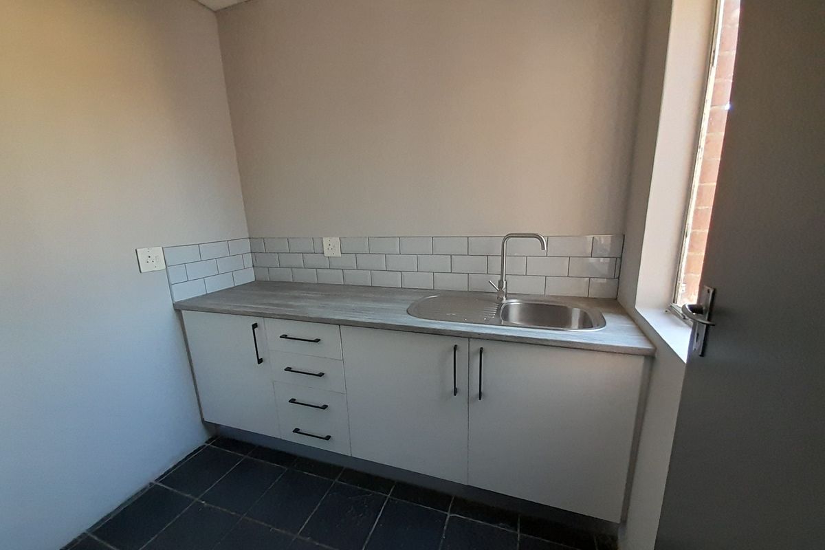 A compact kitchenette area featuring modern white cabinetry, a stainless steel sink, and a subway tile backsplash.
