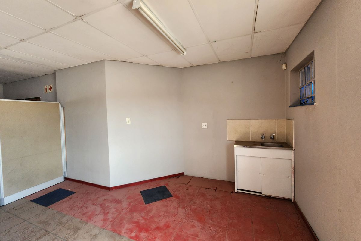 A small office kitchenette area featuring a basic sink unit, tiled flooring, and a suspended ceiling with fluorescent lighting.