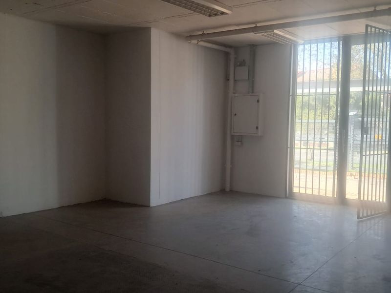 An empty industrial utility space featuring concrete flooring, exposed ceiling piping, and a secure metal gate entrance.