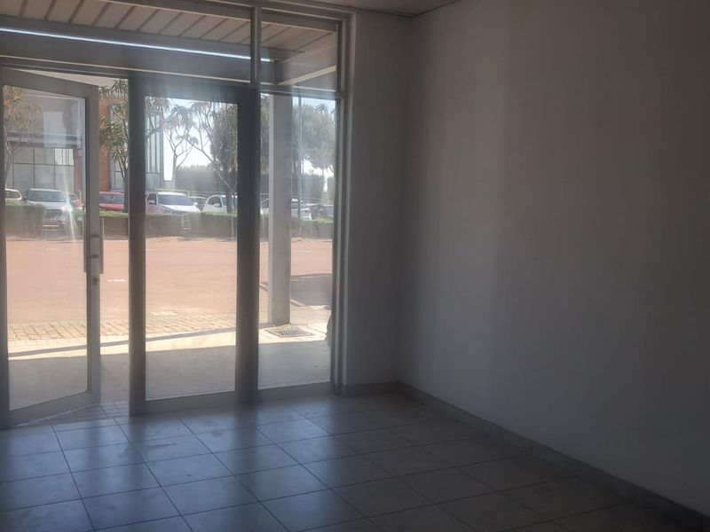 A bright, empty entrance area featuring tiled flooring and large glass doors providing direct access to the exterior parking area.