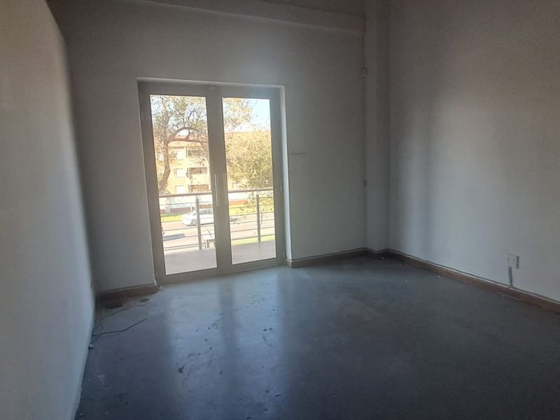 An empty, neutral-toned bedroom featuring a double glass door that provides access to a balcony and allows for natural light.