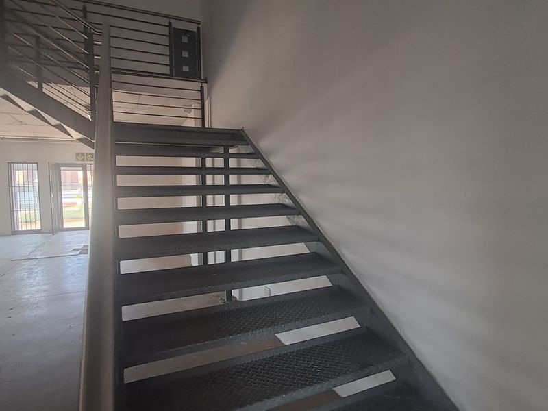 Industrial interior space featuring a metal staircase with balustrade, concrete flooring, and windows fitted with security bars.