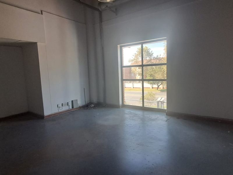 An empty, open-plan office space featuring polished concrete floors and a large grid window providing natural light and street views.
