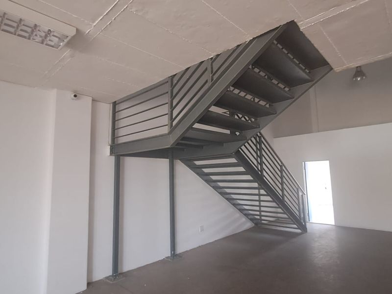 Open plan industrial utility space featuring a prominent metal staircase, concrete ceiling, and functional lighting, suitable for various commercial or storage applications.