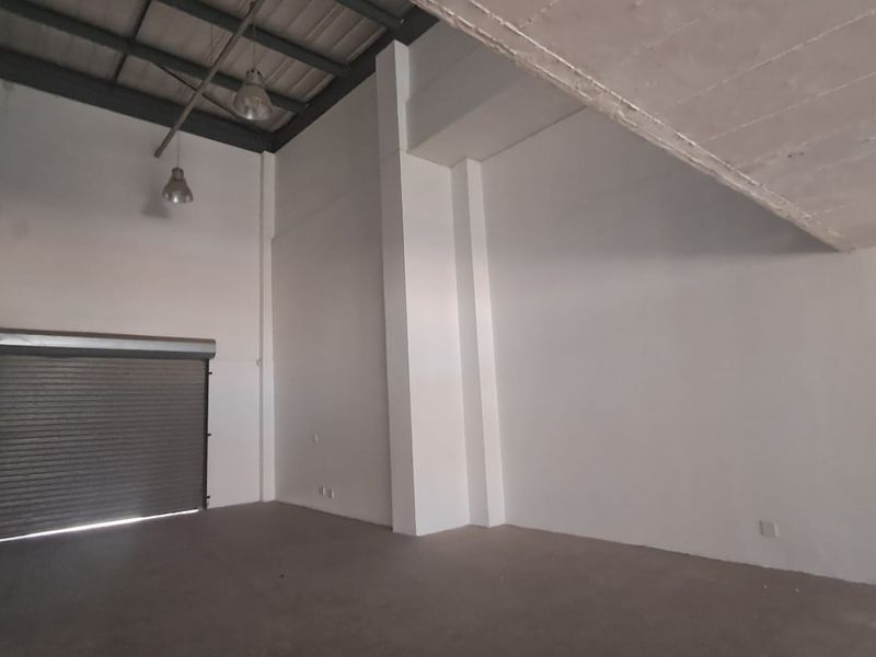 Spacious industrial warehouse unit featuring high ceilings, exposed steel trusses, concrete flooring, and a secure roller shutter door.