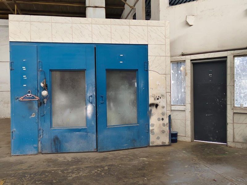Industrial utility space featuring a dedicated spray booth, concrete flooring, and exposed steel roof structure, suitable for workshop or manufacturing operations.