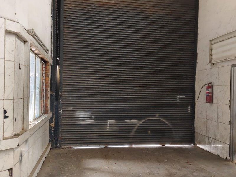 Industrial utility space featuring a large roller shutter door, concrete flooring, and wall-mounted fire safety equipment, suitable for storage or workshop use.