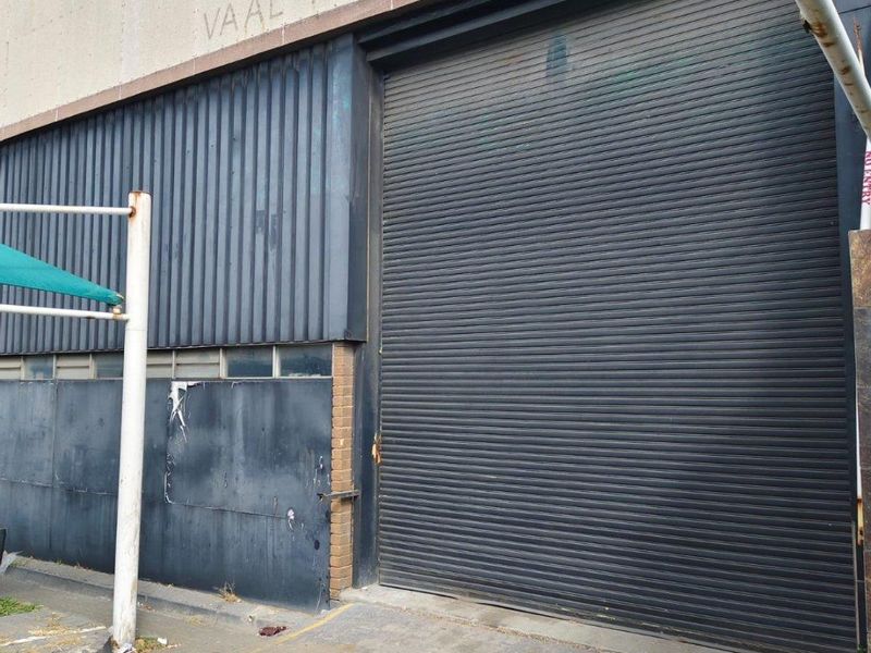 Commercial exterior facade featuring a large industrial roller shutter door and corrugated metal cladding, showing signs of wear and weathering.