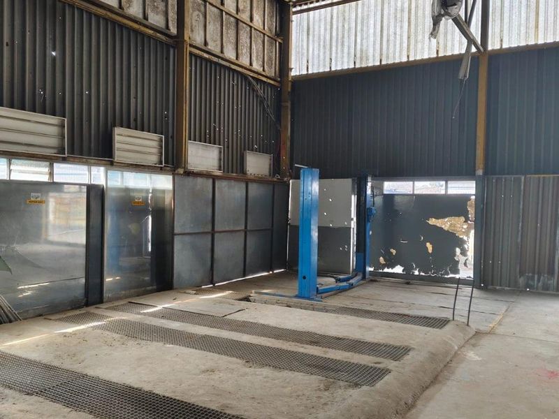 Industrial workshop space featuring a vehicle service pit, single-post lift, and corrugated metal wall cladding, suitable for automotive or commercial maintenance operations.