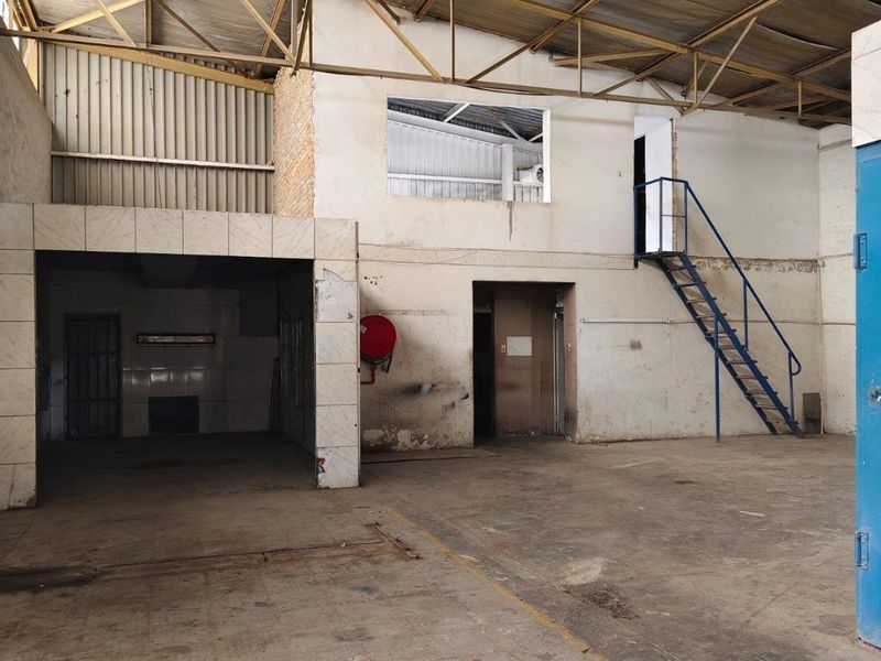 Spacious industrial utility area featuring exposed steel roof trusses, a mezzanine level with metal staircase, and concrete flooring, suitable for various commercial storage or workshop uses.