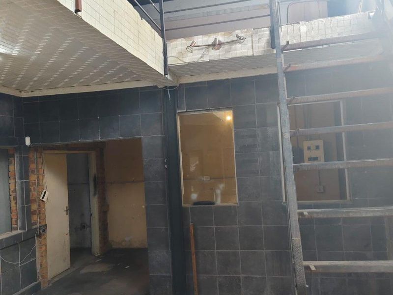 Open plan commercial space featuring a mezzanine level, metal staircase, and tiled wall finishes, currently in need of renovation and refurbishment.