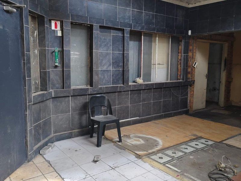 Entrance area featuring dark tiled wall cladding and mixed flooring surfaces in need of repair and refurbishment.