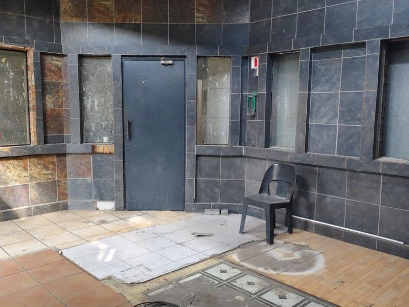 An empty commercial entry area featuring dark tiled wall cladding and mixed flooring surfaces in need of repair and refurbishment.